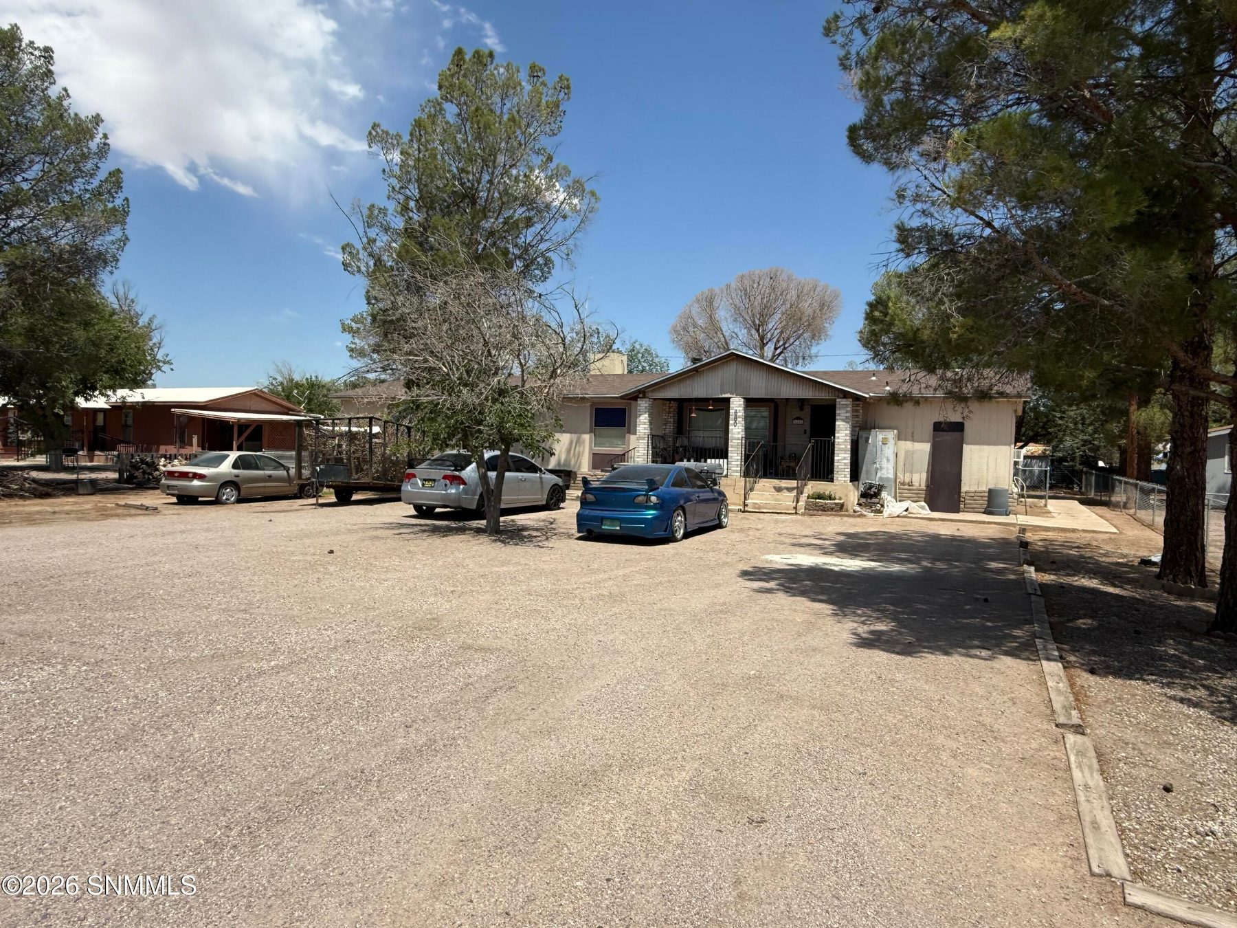 Manufactured home at 660 King Edward Avenue with a gravel driveway, parked cars, and mature pine trees in Las Cruces, New Mexico.