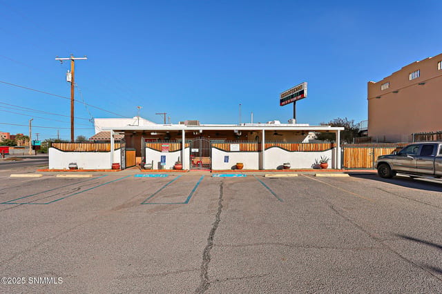 Front exterior of a white stucco adobe commercial building with a covered patio, wrought iron fencing, and a paved parking lot.